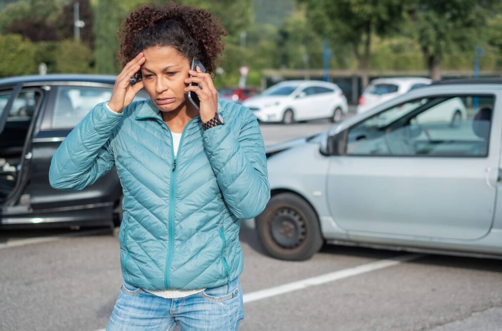 Woman needing a doctor after a car accident - calling on the phone, car accident behind her. 